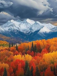 the mountains are covered in colorful trees with snow on top and clouds above them,