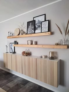 two wooden shelves on the wall with pictures and vases above them in a living room