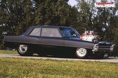 a black car parked on the side of a road next to some grass and trees