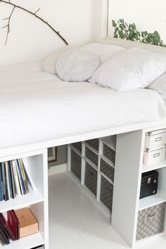 a bed with white sheets and pillows on top of it next to bookshelves