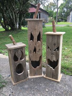 three wooden boxes with carved faces on them sitting in front of some grass and trees