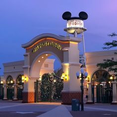 the entrance to an amusement park at night with lights on and mickey mouse heads above it