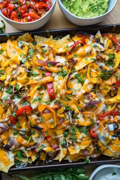 an overhead view of nachos and guacamole with salsa in the background