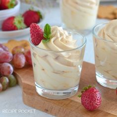 two desserts with whipped cream and strawberries in small glasses on a cutting board