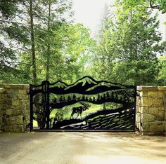 an iron gate with a deer on it in the middle of a driveway surrounded by trees