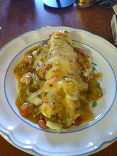 an enchilada on a white plate with blue trim sits on a wooden table