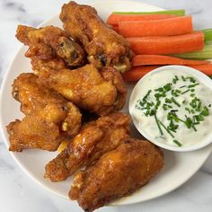 chicken wings with ranch dressing and carrots on a white plate next to celery sticks