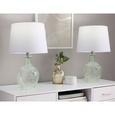 two green glass vases sitting on top of a white table next to a lamp