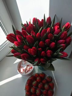 a bouquet of red tulips and strawberries on a white table next to a bowl of yogurt