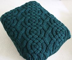 a green knitted cushion sitting on top of a white table next to a pair of scissors