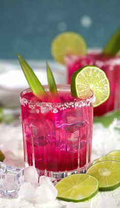 two glasses filled with red liquid and lime wedges on top of ice cubes