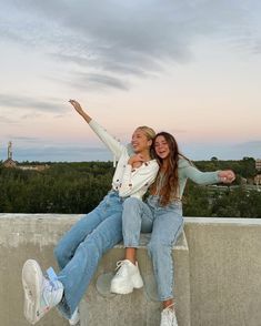 two young women sitting on top of a cement wall