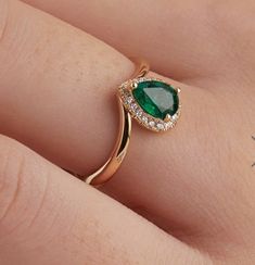 a woman's hand with a green ring on top of her finger and diamond accents around the band