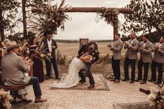 a bride and groom kissing in front of their wedding party at the end of an outdoor ceremony