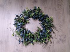 a wreath made out of blue berries and greenery on a wooden floor with wood planks