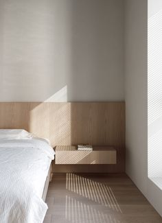 a bed with white sheets and wooden headboard in a room that has sunlight streaming through the window