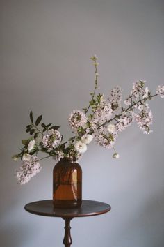 a brown vase with white flowers on top of a table next to a gray wall