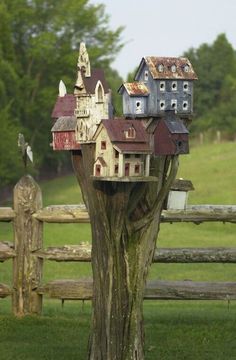 an old tree stump with some little houses on it's top, and a fence in the background