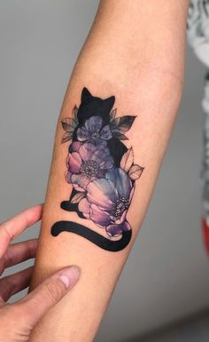 a woman's arm with flowers and a black cat tattoo on the left forearm