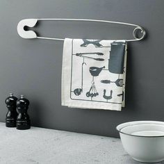 a kitchen towel hanging on the wall next to a white bowl and black pepper shakers