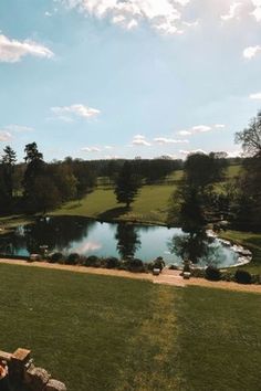 a person sitting on a bench in front of a large pond and grassy area with trees