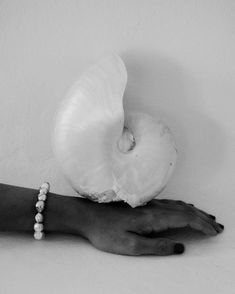 a person's hand with a bracelet holding an onion on their left wrist, against a white wall