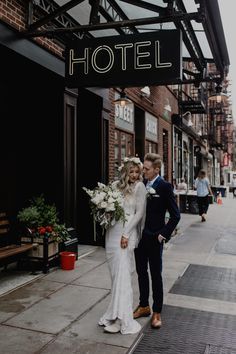 a bride and groom standing on the sidewalk in front of a hotel sign with their arms around each other