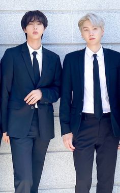 two young men in suits and ties standing next to each other against a stone wall