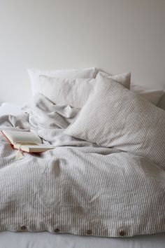 an open book sitting on top of a bed with white sheets and pillows in front of it