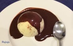 a scoop of ice cream and chocolate sauce on a white plate with a silver spoon