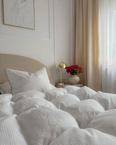 an unmade bed with white comforter and pillows next to a painting on the wall