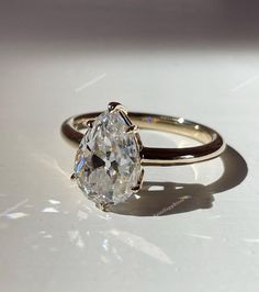 an oval cut diamond sits on top of a white surface with the shadow from the ring