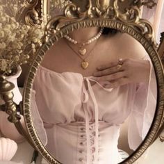 a woman in a white dress is looking at her reflection in a gold framed mirror