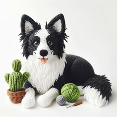 a black and white dog is sitting next to some crocheted cacti