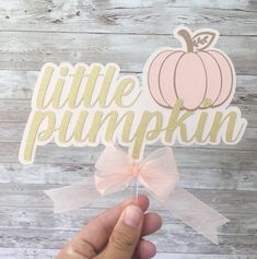 a hand holding up a little pumpkin cutout on top of a wooden table with a pink bow