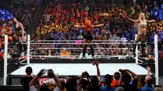 two women standing on the edge of a wrestling ring in front of an audience with their arms outstretched