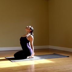 a woman sitting on a yoga mat in the middle of a room with her eyes closed