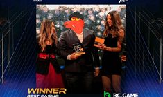 two women standing next to a man in a suit and tie holding an award for best casino game