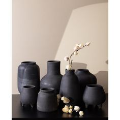 several black vases with flowers in them on a table next to a white wall