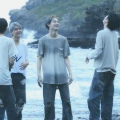 four young men standing next to each other near the ocean