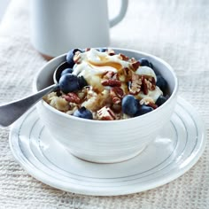 a bowl filled with fruit and nuts on top of a white plate next to a cup