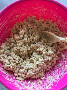 a pink bowl filled with macaroni and cheese on top of a table next to a wooden spoon