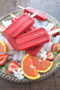 popsicles and oranges are on a platter with ice cubes, strawberries, and flowers