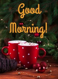 two red mugs filled with coffee sitting on top of a wooden table next to christmas decorations