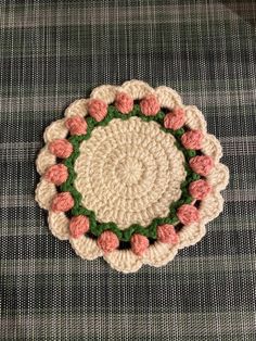 a crocheted doily with pink flowers in the center on a plaid cloth