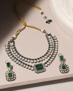 Presenting a captivating two-layer Polki set featuring a stunning emerald Polki stone at its center, accompanied by matching earrings. This ensemble exudes drama and elegance, perfect for adding a touch of regal charm to any occasion. Finish: Rhodium Material: Brass, Polkis & Emerald Stones Color: White, Green Size: Free Size, Adjustable Closure Type: Draw String Box Contains: 1 Necklace, 1 Pair of Earrings Elegant Emerald Kundan Necklace With Stone Work, Elegant Kundan Necklace With Emerald Stone Work, Elegant Emerald Kundan Necklace For Festive Occasions, Elegant Kundan Emerald Necklace For Festive Occasions, Elegant Emerald Jewelry With Stone Work, Elegant Emerald Necklace With Stone Work, Elegant Green Kundan Necklace For Festive Occasions, Festive Hand Set Emerald Necklace, Elegant Kundan Hand Set Emerald Necklace