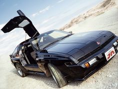 a black car with its door open sitting in the desert