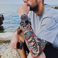 a man with a tattoo on his arm sitting by the water