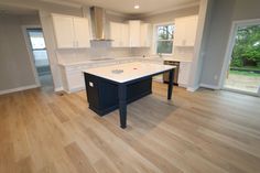 an empty kitchen with white cabinets and black island in the foreground, wood flooring on the other side