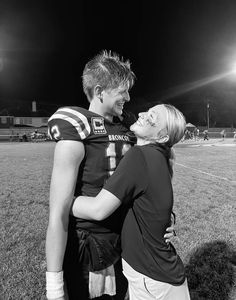 a man and woman embracing each other on a football field at night with lights in the background